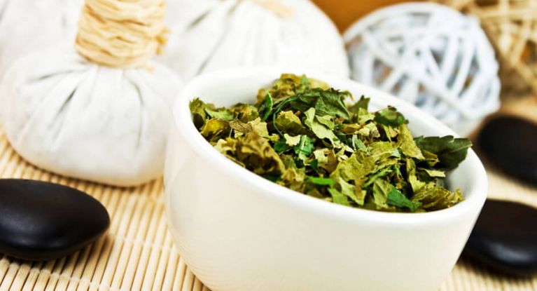 Kräuterstempel und getrocknete Kräuter in einer weißen kleinen Schale