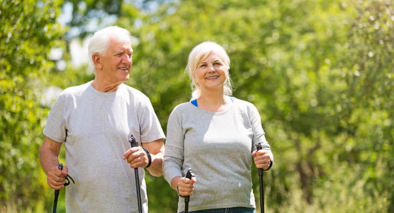 ein älteres Paar spaziert mit Nordic-Walking-Sticks im Wald