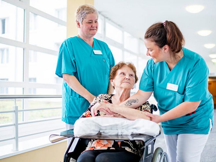 Weibliche Pflegekräfte schieben eine Patientin im Rollstuhl