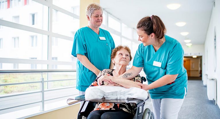 Weibliche Pflegekräfte schieben eine Patientin im Rollstuhl