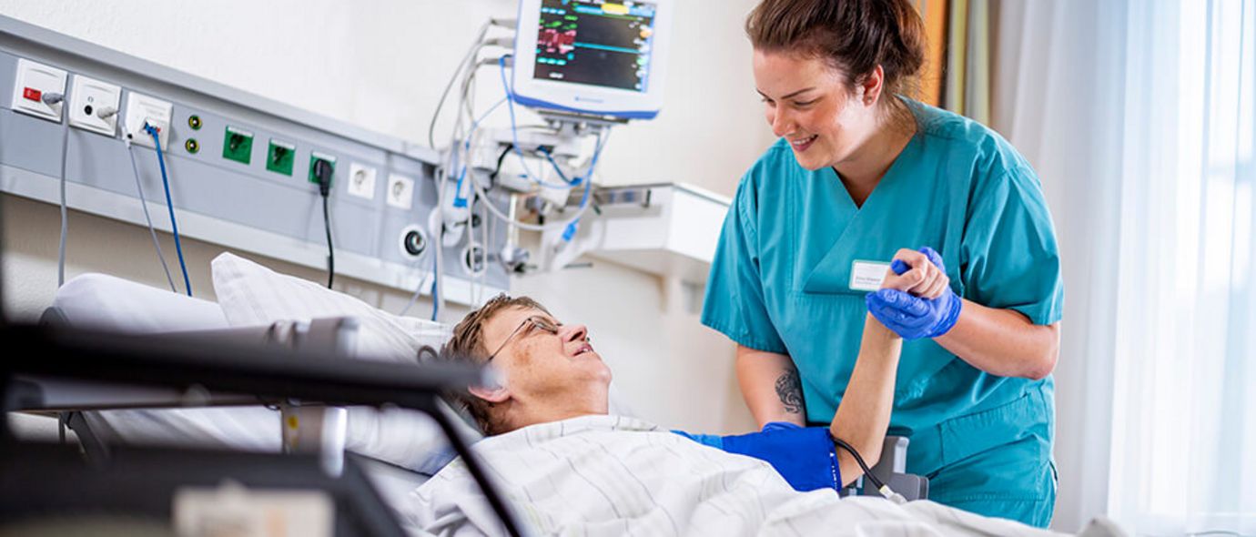 Weibliche Pflegekraft spricht mit im Bett liegenden Patienten