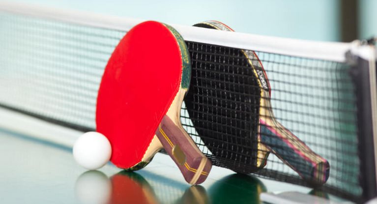 ein roter und ein schwarzer Tischtennisschläger mit einem weißen Ball am Tischtennisnetz auf der Tischtennisplatte